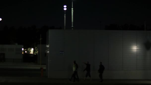 Os jovens vão no fundo da parede de rua à noite. Imagens de stock. Os jovens voltam para casa tarde no fundo da parede iluminada por lanterna — Vídeo de Stock