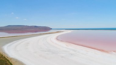 Kırım'da turuncu göl. Atış. Beyaz kuma karşı parlak turuncu göl suyunun üst görünümü. Mavi gökyüzünün arka planında beyaz kum üzerinde renkli turuncu su dünya dışı manzara