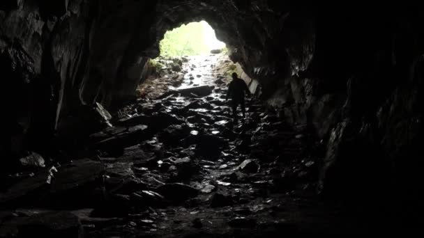 Pelancong turun ke gua. Rekaman saham. Traveler menjelajahi terowongan gua yang menuruni tali. Terowongan gua yang berbahaya, licin dari lembab dan mengilhami rasa takut kegelapan yang tidak diketahui — Stok Video