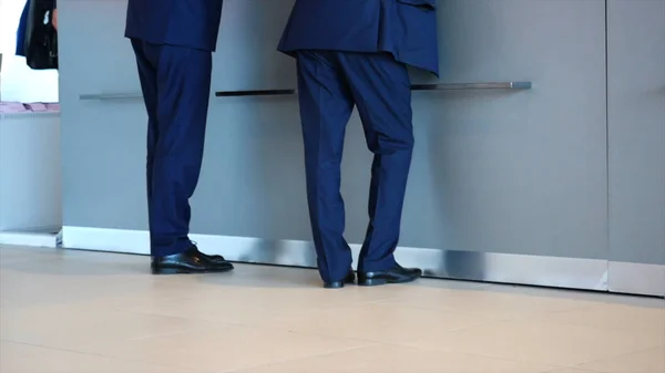 青いズボン、スーツジャケット、黒い靴を着た2人のビジネスマンが受付に立ち、何かを尋ねる。メディア。ビジネスと管理の概念 — ストック写真