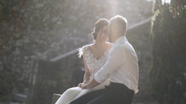 Gün ışığında oturan güzel yeni evliler. Eylem. Güzel gelin ve damat oturup birbirlerine parlak güneş ışığı ile aydınlatılmış bakmak. Gençlerin samimi ve şefkatli sevgisi