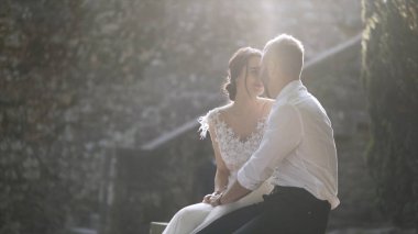 Gün ışığında oturan güzel yeni evliler. Eylem. Güzel gelin ve damat oturup birbirlerine parlak güneş ışığı ile aydınlatılmış bakmak. Gençlerin samimi ve şefkatli sevgisi
