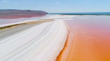 Kırım'da turuncu göl. Atış. Beyaz kuma karşı parlak turuncu göl suyunun üst görünümü. Mavi gökyüzünün arka planında beyaz kum üzerinde renkli turuncu su dünya dışı manzara