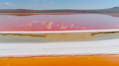 Bulutların üst görünümü pembe göle yansıdı. Atış. Parlak renkli turuncu ve pembe göller beyaz kıyı ile ayrılır. Pembe gölde bulutların ve mavi gökyüzünün güzel yansıması