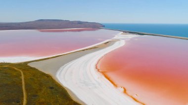 Mavi deniz arka plan üzerinde pembe göllerüst görünümü. Atış. Pembe ve turuncu renklerden oluşan parlak renkli göller, mavi denizden beyaz kıyılarla ayrılmıştır. Pembe göllerin doğal fenomeni