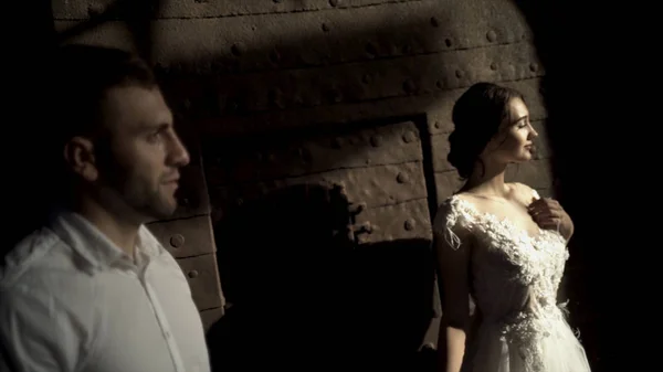 Les amoureux regardent le soleil de réunion. L'action. Les jeunes mariés dans la chambre noire attendent avec impatience la lumière du soleil. Belle mariée en robe blanche regarde romantiquement la lumière du soleil chaud — Photo