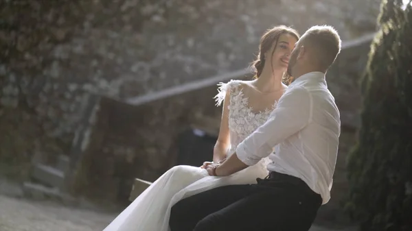 Beautiful newlyweds sitting in sunlight. Action. Beautiful bride and groom sit and look at each other illuminated by bright sunlight. Sincere and tender love of young people — Stock Photo, Image