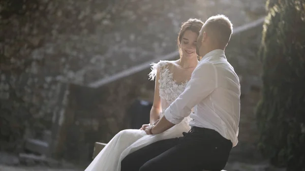 Beautiful newlyweds sitting in sunlight. Action. Beautiful bride and groom sit and look at each other illuminated by bright sunlight. Sincere and tender love of young people — Stock Photo, Image