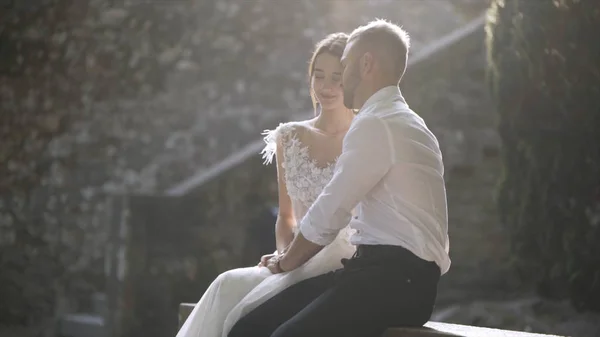 Beautiful newlyweds sitting in sunlight. Action. Beautiful bride and groom sit and look at each other illuminated by bright sunlight. Sincere and tender love of young people — Stock Photo, Image