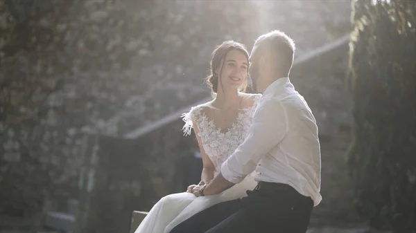 Beautiful newlyweds sitting in sunlight. Action. Beautiful bride and groom sit and look at each other illuminated by bright sunlight. Sincere and tender love of young people — Stock Photo, Image