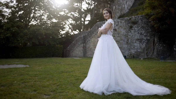 Ortaçağ duvarlarının arka planda güzel gelin. Eylem. Ağaçların arka planda yeşil çim üzerinde poz beyaz elbiseli Gelin. Gelin yeşil bahçede gelinlik şefkatle gülümsüyor