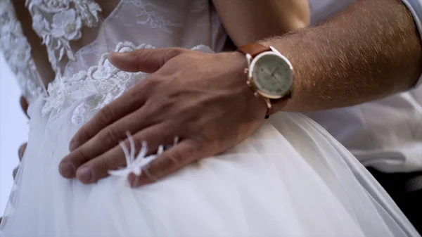 Κοντινό-up των συζύγων χέρια αγκαλιάζοντας τη γυναίκα. Δράση. Ο σύζυγος αγγίζει απαλά τη μέση των συζύγων του σε λευκό νυφικό. Έννοια του γάμου — Φωτογραφία Αρχείου