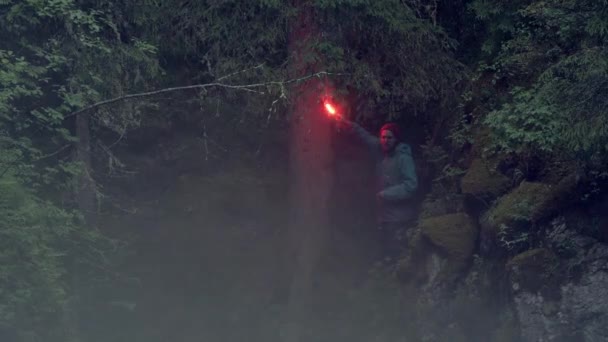 赤信号火災ストック映像。ハイカーはハイキング中に森の中で道に迷い、今は赤いフレアを振っています。旅行者の波は暗い森の中に煙の多くを残して火災を合図します — ストック動画
