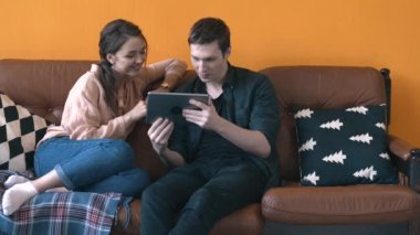 Evde kanepede oturan ve tablet ekranına izlerken mutlu genç çift in yakın çekim görünümü. Stok görüntüleri. Erkek ve kadın kanepede rahatlatıcı, mutlu hafta sonu