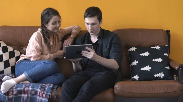 Vista de cerca de la feliz pareja joven sentada en el sofá en casa y mirando a la pantalla de la tableta. Imágenes de archivo. Hombre y mujer relajándose en el sofá, feliz fin de semana — Foto de Stock