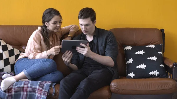 Vista de cerca de la feliz pareja joven sentada en el sofá en casa y mirando a la pantalla de la tableta. Imágenes de archivo. Hombre y mujer relajándose en el sofá, feliz fin de semana — Foto de Stock