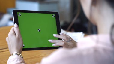 Pembe gömlekli genç kadının omzundan masada oturan ve kroma anahtar yeşil ekranda tabletüzerinde kayan görünümü. Stok görüntüleri. Kendi içeriğinizin yerleştirilmesi için Renk anahtar ekranı.