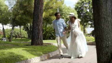 Yeni evliler yazın parkta koşarlar. Eylem. Güzel sevgi dolu çift romantik parkta el ele tutuşarak kaçmak. Beyaz elbiseli karısı kocasını güneş ışığıyla aydınlatarak tutuyor
