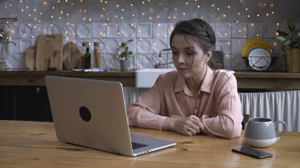 Крупный план привлекательной молодой женщины, работающей за ноутбуком, сидя на кухне. Запись. Современный декорированный интерьер дома на заднем плане — стоковое фото