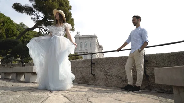 Beautiful young couple on honeymoon. Action. Husband admires his beautiful young wife whirling in white dress. Newlyweds on background of stone observation deck — Stock Photo, Image