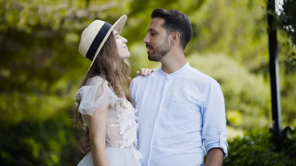 Lovely young couple admiring each other. Action. Newlyweds stand in embrace against each other and throw gentle glances. Couple stand in embrace against green park on honeymoon — Stock Photo, Image