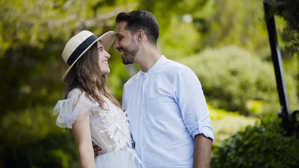 Bella giovane coppia che si ammira. Azione. Gli sposi si abbracciano l'uno contro l'altro e gettano dolci sguardi. Coppia stand in abbraccio contro parco verde in luna di miele — Foto Stock