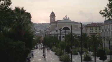 Palmiye ağaçları ile parkın arka planda Kilise. Eylem. Palmiye ağaçları ve kilise bakan yürüyüş insanlar ile şehir küçük bir park. Parkta yürüyen turistler ile Güney Avrupa kenti