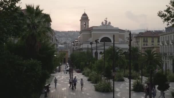 Chiesa sullo sfondo del parco con palme. Azione. Città piccolo parco con palme e persone a piedi con vista sulla Chiesa. Città dell'Europa meridionale con turisti a piedi nel parco — Video Stock