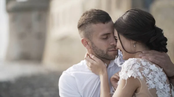 Close-up de noiva de conto de fadas bonita em um vestido de noiva branco na moda e noivo sentado no banco, sorrindo e beijando. Acção. Um casamento de livro de histórias — Fotografia de Stock