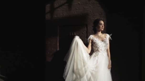 古い暗い壁や門の近くに立って、笑顔のファッショナブルな白いウェディングドレスで若い美しい花嫁のクローズアップビュー。アクション。ストーリーブックの結婚式 — ストック動画