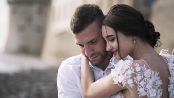Κοντινό πλάνο της όμορφης παραμυθένιας νύφης με ένα μοντέρνο λευκό νυφικό και γαμπρό που κάθεται στον πάγκο, χαμογελώντας και φιλώντας. Πάμε. Ένας γάμος παραμυθιού — Αρχείο Βίντεο