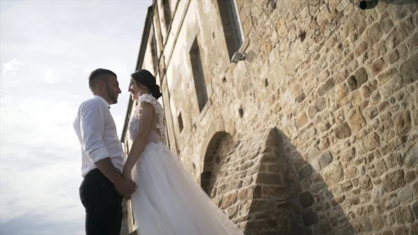 Όμορφο παραμυθένιο ζευγάρι που ποζάρει κοντά σε παλιό τοίχο κάστρου. Δράση. Ο κομψός γαμπρός κρατώντας τα χέρια της αξιαγάπητα νύφη. — Φωτογραφία Αρχείου