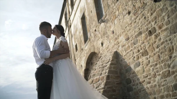 Όμορφο παραμυθένιο ζευγάρι που ποζάρει κοντά σε παλιό τοίχο κάστρου. Δράση. Ο κομψός γαμπρός κρατώντας τα χέρια της αξιαγάπητα νύφη. — Φωτογραφία Αρχείου