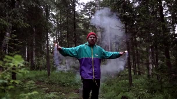 Man and colored smoke bombs in forest. Stock footage. Young man lit smoke colored checkers in forest for beautiful photography — Stock Video