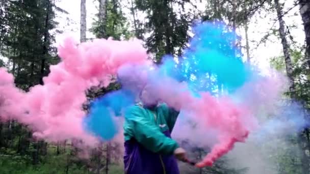Homem com bombas de fumo coloridas na natureza. Imagens de stock. Jovem espalha córregos de damas de fumaça coloridas em floresta densa — Vídeo de Stock