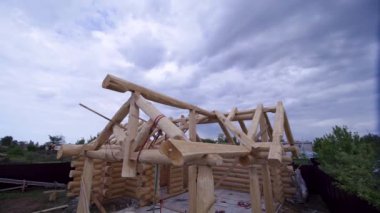 Vinçli kır evi inşaatında çalışanlar. Şarjör. Köy ahşap evinin inşaatı. Ahşap dizaynlı yapıcılar mavi gökyüzünün arka planında vinç kirişleri taşıyorlar.