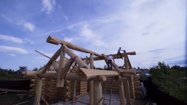 Constructores que trabajan en la construcción de casa de madera. Clip. La construcción de la casa de madera de los troncos con los trabajadores sobre el fondo del cielo azul — Vídeos de Stock