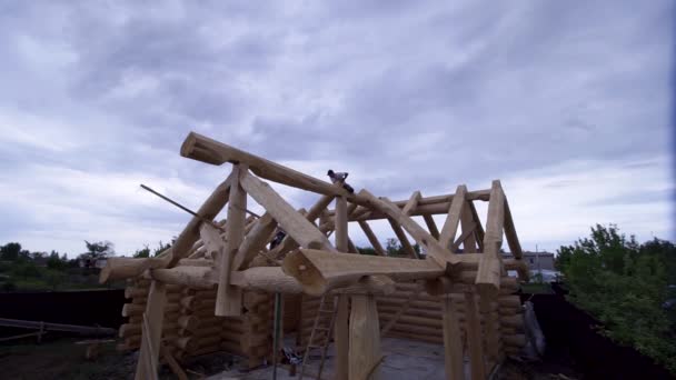 Builders working on construction of wooden cottage. Clip. Construction of wooden house of logs with working workers on background of cloudy sky — Stock Video