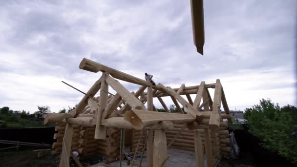 Bau einer hölzernen Landhaus. Clip. Kran hebt Baumstamm an im Bau befindlichem Holzhaus Struktur des im Bau befindlichen hölzernen Landhauses — Stockvideo