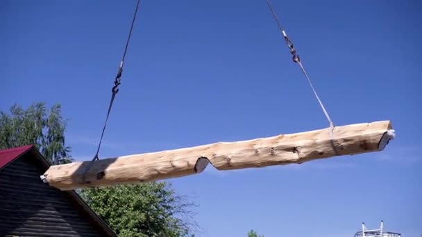 Kran hebt Holz auf Baustelle. Clip. Bauprozess mit dem Heben schwerer Balken mittels Kran. Kranaufzüge behandeltes Baumstamm auf Himmel Hintergrund — Stockvideo