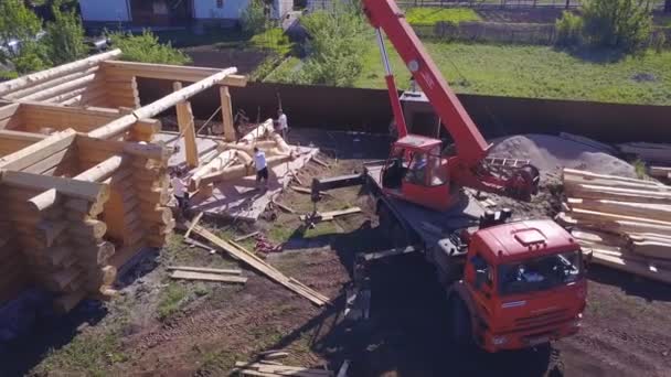 Grue et les travailleurs à la construction de la maison en bois. Clip. Vue du dessus du processus de travail avec une équipe de travailleurs pour construire une maison de campagne en bois — Video