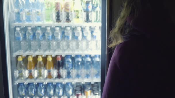 Vista desde la parte posterior de la mujer joven en abrigo púrpura elegir una bebida de la máquina expendedora. Imágenes de archivo. Máquina expendedora de bebidas que vende agua en botellas — Vídeo de stock
