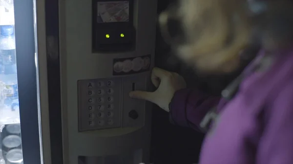 View from the shoulder of young woman inserting coins to vending machine. Stock footage. Beverage vending machine selling water in bottles