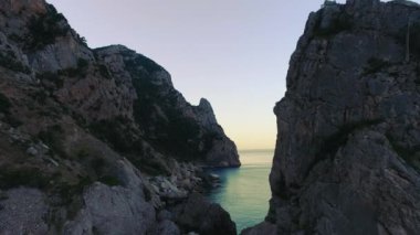 Gökyüzü arka planında mavi deniz olan yaban kayalıkların üst görüntüsü. Vuruldu. Mavi denizin sakin sularıyla kayalık kıyılar gökyüzünün arka planında ufka ulaşıyor.