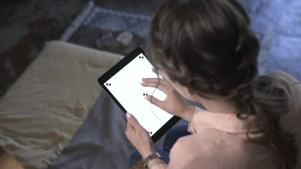 Pohled na mladou ženu s hnědými vlasy, které sedí na židli, drží iPad, zadáváním a klouže na bílou obrazovku chromatu. Skladní záběry. Nový koncept technologie smartphone — Stock video