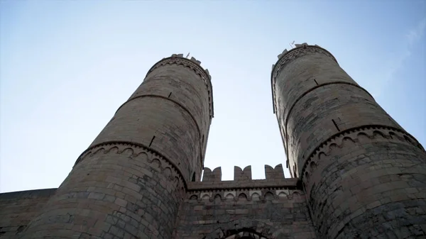 Bottom view of old fortress towers. Action. Two towers of old castle rise on background of blue sky. Beautiful and powerful view of ancient construction of fortress towers