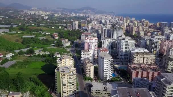 Вид сверху курортного зеленого города на фоне моря и гор. Клип. Красивый пейзаж с зелеными растениями среди курортных высотных зданий города на побережье — стоковое видео