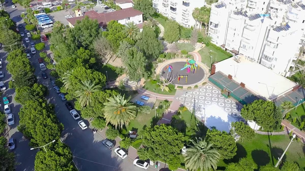 Zona de ciudad turística con parque infantil. Clip. Vista superior de la ciudad turística del sur con zona ajardinada con parque infantil. Parque infantil cerca de edificios residenciales de gran altura en el sur de la ciudad en verano — Foto de Stock