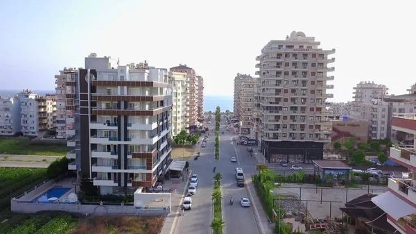 Top view of city road leading to sea. Clip. Road passing among high-rise buildings of city leads to sea on horizon. Top view of straight road among hotels of resort town by sea