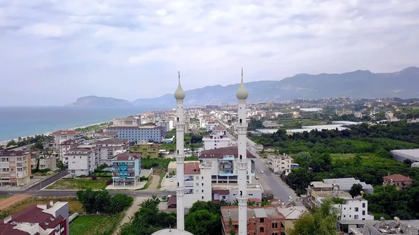 Top view of white towers of mosque. Clip. Beautiful high towers of mosque on background of coastal city with blue sea. Resort town with white mosque. Muslim religion